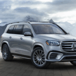 Front-side view of a silver Mercedes-Benz SUV parked on a mountaintop patio with misty peaks in background.